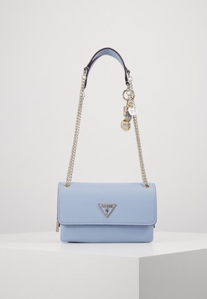 Sac à main Guess en cuir bleu clair avec bandoulière chaîne argentée et charms logo, placé sur une surface blanche avec un fond uni.
