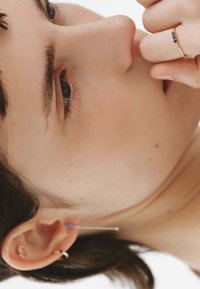 Pendientes de oro con un diseño circular y un anillo de piedra preciosa azul. Se pueden ver la piel suave y el cabello oscuro, mostrando los detalles de la joyería.
