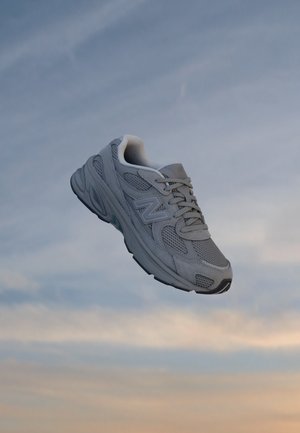 Grå New Balance løbesko, der hænger mod en skyet aftenhimmel.