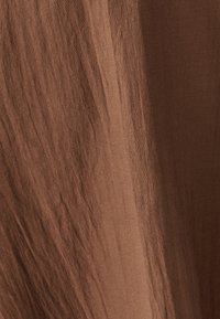 Rjav tekstil z gladko teksturo in subtilnim sijajem, ki vsebuje mehke, tekoče linije in rahlo nagubano površino.