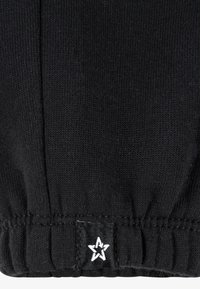 Black knitted fabric with a gathered hem, featuring a small white star logo label. Texture appears smooth and stretchy.