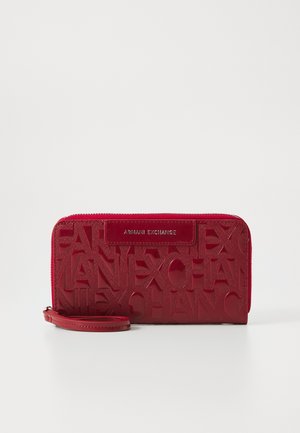 Κόκκινο δέρμα πορτοφόλι με ανάγλυφο λογότυπο. Διαθέτει φερμουάρ κλεισίματος, αποσπώμενο λουρί καρπού και γυαλιστερή επιφάνεια.