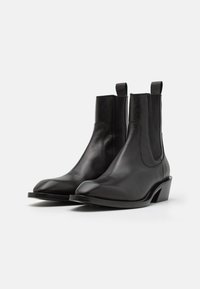 Botas de cuero negro hasta el tobillo con un diseño de punta afilada, paneles laterales elásticos y un bajo tacón cuadrado. Textura suave con una silueta elegante.