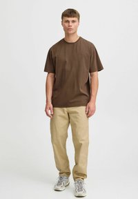 Camiseta corta marrón de algodón con cuello redondo. Combinada con pantalones beige claros y zapatillas deportivas de color claro.