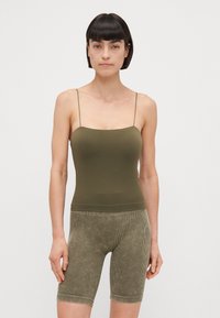 Un débardeur vert olive avec des bretelles fines, associé à un short en olive vert texturé et côtelé. Les deux vêtements ont une coupe ajustée et un tissu doux.