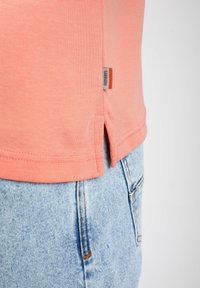 Rosa bomullströja i stickad kvalitet med sidöppningar och en synlig varumärkesetikett. Matchad med ljusblå denimshorts med kontrastsöm.