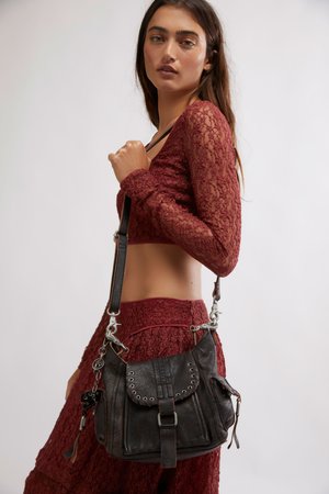 Jeune femme portant un ensemble assorti composé d'un crop top en dentelle bordeaux et d'une jupe, portant un sac à bandoulière en cuir noir avec des œillets métalliques et une boucle.