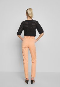 Svart perforerad stickad topp med trekvartsärmar, kombinerad med ljus persikofärgade slim-fit byxor och svarta klacksandaler.