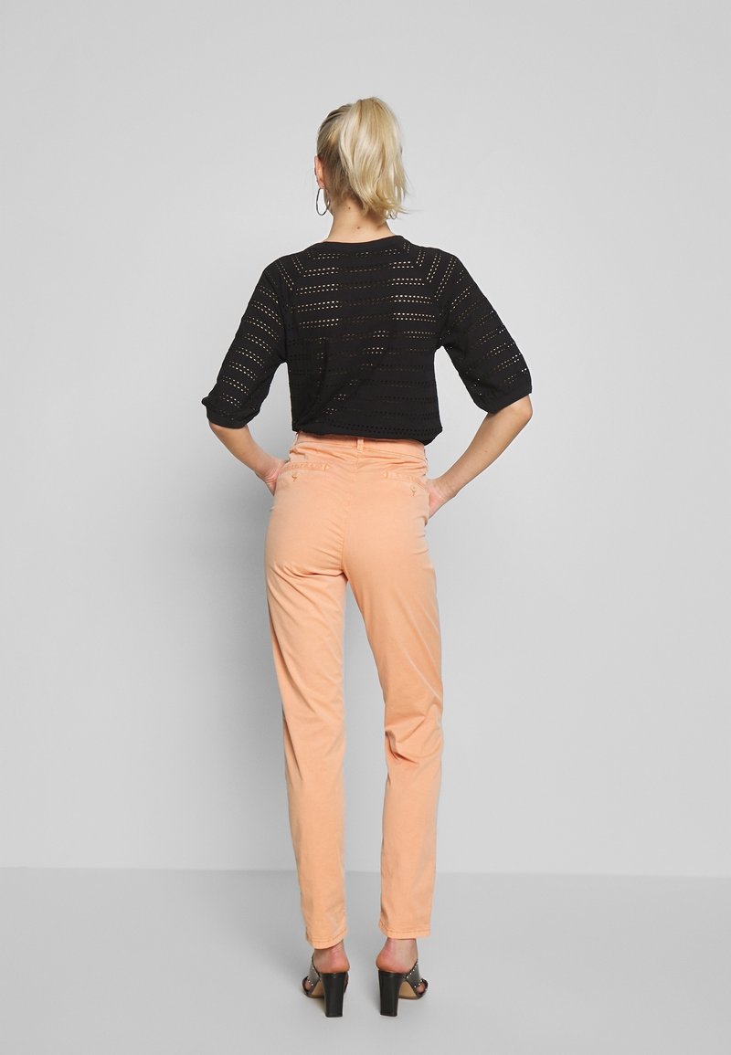 Svart perforerad stickad topp med trekvartsärmar, kombinerad med ljus persikofärgade slim-fit byxor och svarta klacksandaler.