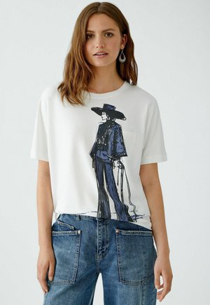 Weißes T-Shirt mit blauer grafischer Illustration einer Figur mit Hut, kombiniert mit blauen Jeans in Übergröße mit großen Taschen. Weicher Stoff.