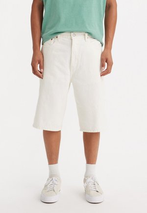 Bermuda din denim alb, cu o croială dreaptă, având închidere cu buton și fermoar. Purtați cu un tricou verde și pantofi de culoare deschisă.