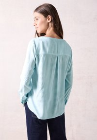 Camicia azzurro chiaro a maniche lunghe con righe verticali bianche, vestibilità comoda, dettaglio con piega sul retro e scollatura tonda. Tessuto morbido.