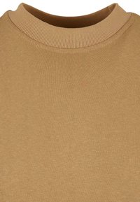 Gros plan d'un pull en tricot marron chameau avec un col rond côtelé et une texture de tissu lisse.
