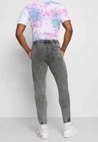 Šedé jogger kalhoty s elastickým pasem a manžetami u kotníků, se zadní kapsou. Nosit s tričkem s krátkým rukávem ve stylu tie-dye.