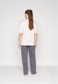 Ljusrosa t-shirt i bomull med korta ärmar, avslappnad passform, bärs med grå vida byxor. Håret är uppsatt i en lång hästsvans.