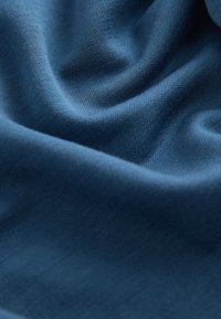 Tumši zils audums ar gludu tekstūru un smalku pinuma rakstu, viegli krītot ar maigiem locījumiem un krokām.