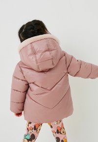 Pudret pink jakke med hætte, der har en blød faux fur krave og chevron syningsdesign. Bæret med mønstrede leggings.