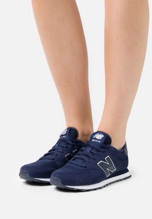 Chaussures de sport bleu marine en suède et mesh, dotées d'une semelle blanche, d'un col rembourré et d'accents réfléchissants sur le logo et les œillets.
