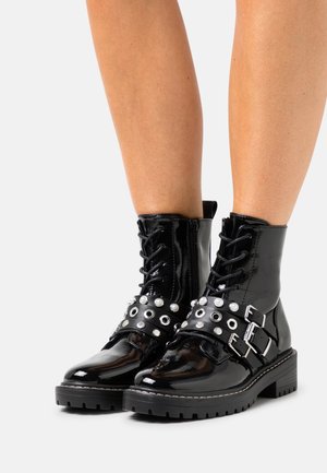 Bottines en cuir verni noir avec fermeture à lacets sur le devant, brides cloutées, détails en métal argenté et semelle épaisse.