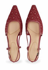 Chaussures en tissu tissé rouge avec un bout pointu et des côtés découpés, dotées d'une fine sangle à la cheville et d'une doublure intérieure beige. Motif texturé sur l'ensemble.