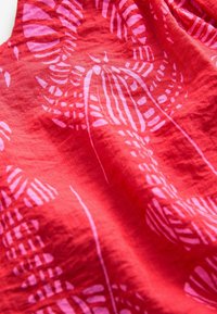 Tissu rouge avec motif botanique rose, présentant une surface texturée et un tombé doux. Détail de couture visible le long des bords.