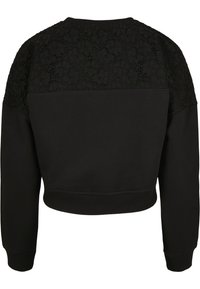 Felpa nera corta con maniche lunghe, caratterizzata da una texture in pizzo sulle spalle. Tessuto liscio con collo e orlo a coste.