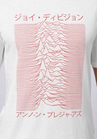 Balta marškinėliai su raudonu linijų grafiku, vaizduojančiu sluoksniuotų bangų formas, su japonų kalbos tekstu virš ir apačioje dizaino.