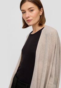 Beige cardigan gemaakt van zachte stof, open voorkant ontwerp, losse pasvorm, gecombineerd met een zwart ribbel top, benadrukt gelaagde texturen.