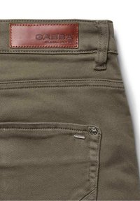 Az olívazöld pamutnadrágon bőr címke látható dombornyomott szöveggel. Egy fém szegecs is megfigyelhető a zseb közelében, amely részletgazdagításként szolgál a dizájnban.