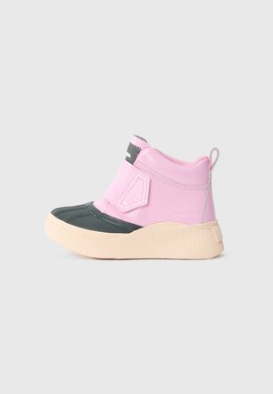Botte de cheville imperméable pour enfant avec un dessus rose, un capot noir, une semelle beige et une fermeture à bande Velcro sur un fond uni.