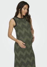 Tamsiai žalia nėštumui skirta suknelė su tekstūruotu bangų raštu, be rankovių dizainu ir kontrastingu juodu apykaklė. Prigludusi siluetas.