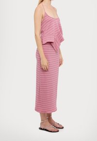 Abito a righe rosa con uno strato superiore fluente e una gonna aderente. Presenta spalline sottili e lunghezza fino alla caviglia, abbinato a sandali metallici.