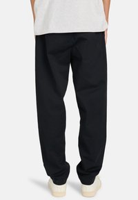 Zwarte katoenen broek met een losse pasvorm, rechte pijpen en zichtbare stikdetails, gecombineerd met witte sneakers.