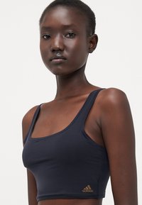 Tamno plavi sportski crop top od glatkog materijala, s izrezom u obliku lopte, uskim trakama i malim zlatnim Adidas logom na rubu.