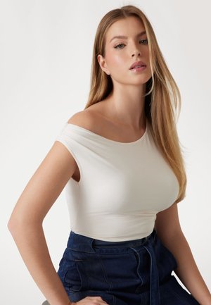 Balti off-the-shoulder marškiniai, pagaminti iš lygaus audinio, su trumpomis rankovėmis, derinami su aukštu liemeniu mėlynomis džinsinėmis šortais.