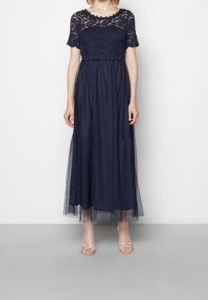 Robe maxi bleu marine avec un haut en dentelle à manches courtes, un corsage ajusté et une jupe en tulle fluide. Les accents comprennent une superposition transparente.