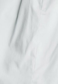 Gros plan sur un tissu blanc montrant une texture lisse avec une couture verticale prononcée et des ombres légères et subtiles.