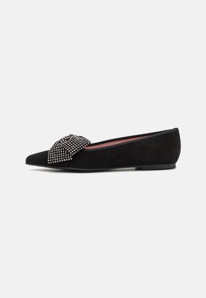 Chaussure plate noire à bout pointu avec un grand nœud clouté argenté sur le devant et un petit talon.