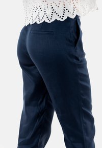 Pantaloni blu navy con una texture liscia, dotati di due tasche laterali, una vestibilità sartoriale e un design classico che arriva alla caviglia.
