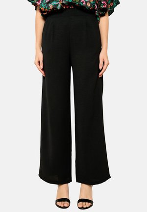 Zwarte wijde broek van een textuurstof, met een hoge tailleband en plooien, gestyled met een gebloemde top en zwarte sandalen.