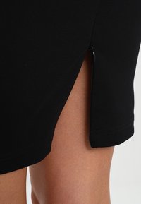 Černá upnutá sukně s bočním zipem, s hladkou texturou a lemem, který sahá těsně nad koleno, zdůrazňující elegantní design.