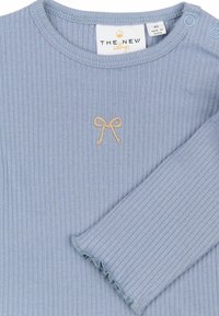 Top de manga larga de color azul claro con textura de canalé y escote redondeado. Presenta un lazo beige bordado y botones a presión en el hombro para facilitar el vestir.