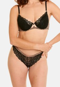 Soutien-gorge en dentelle noire avec une bande en imprimé léopard, doté de bords festonnés et d'un fermoir décoratif sur le devant. String en dentelle assorti avec des détails similaires.