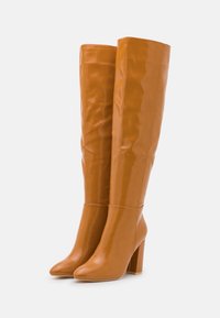 Botas altas de cuero marrón brillante con un diseño ajustado, punta redonda y tacón grueso, que exhiben una textura suave y acentos mínimos.
