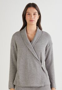 Grijze, geribbelde cardigan met een sjaalkraag, lange mouwen en een knoopsluiting aan de zijkant. Zachte textuur met een ontspannen pasvorm.