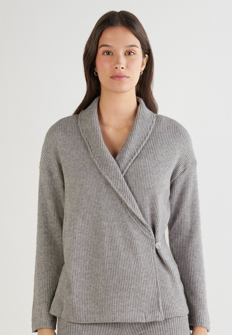 Grijze, geribbelde cardigan met een sjaalkraag, lange mouwen en een knoopsluiting aan de zijkant. Zachte textuur met een ontspannen pasvorm.