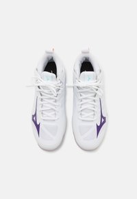 Vita idrottsskor i vitt med meshpaneler, lila accenter och svarta innersulor. Har vita snören och en dragöglan med en orange detalj.