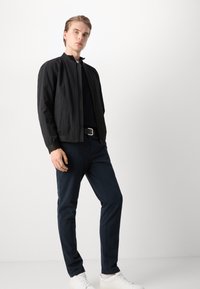 Black bomber jacket with a zip front, ribbed cuffs, and collar; paired with navy trousers and white sneakers. Smooth, lightweight fabric.