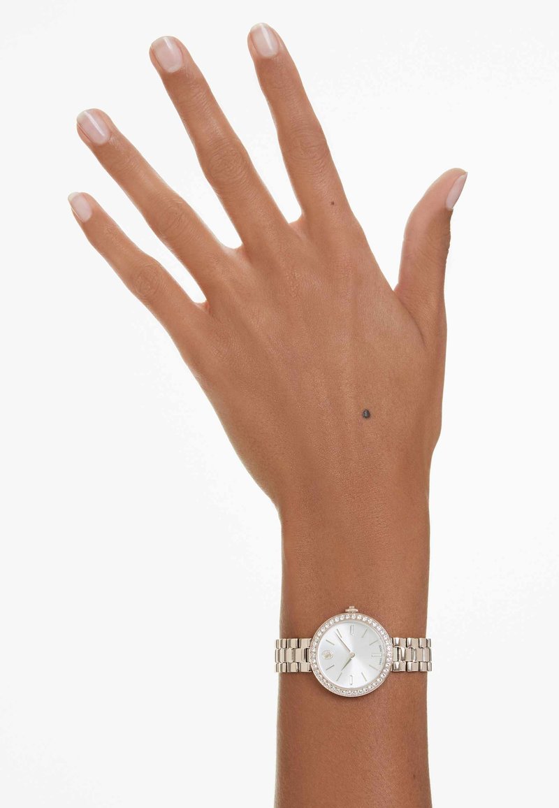 Montre bracelet en argent avec un cadran rond, un cadran blanc, des accents en cristal et un bracelet en maillons métalliques, présentée sur une main à la peau claire.