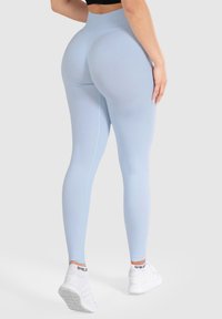 Světlomodré legíny s vysokým pasem, hladkým materiálem a přiléhavým střihem, doplněné bílými sportovními botami.